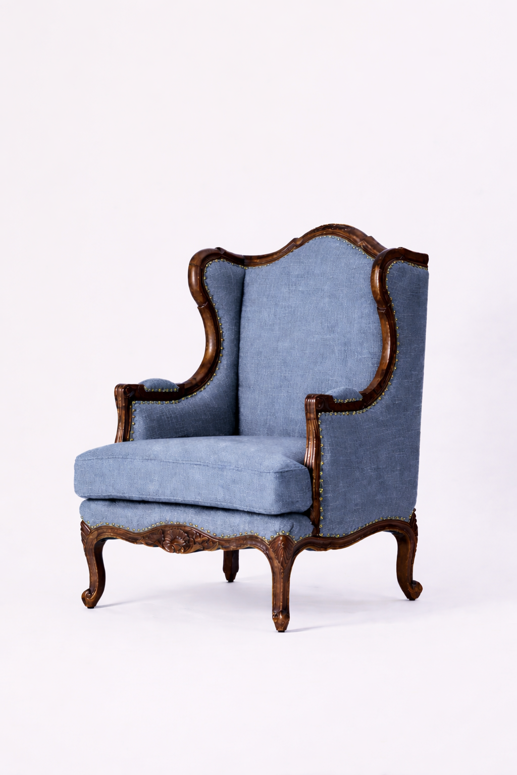 The Montclair Heritage Wingback Armchair is a handcrafted solid wood chair with ornate curved legs and arms, light blue upholstery, a high slightly winged back, and a cushioned seat, shown against a plain white background.