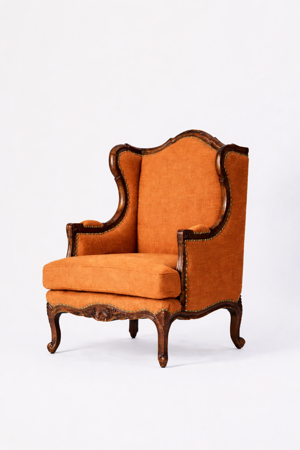 The Montclair Heritage Wingback Armchair showcases orange upholstery, a handcrafted solid wood frame, curved armrests, a high back, and cabriole legs in an ornate vintage style, set against a plain white background.