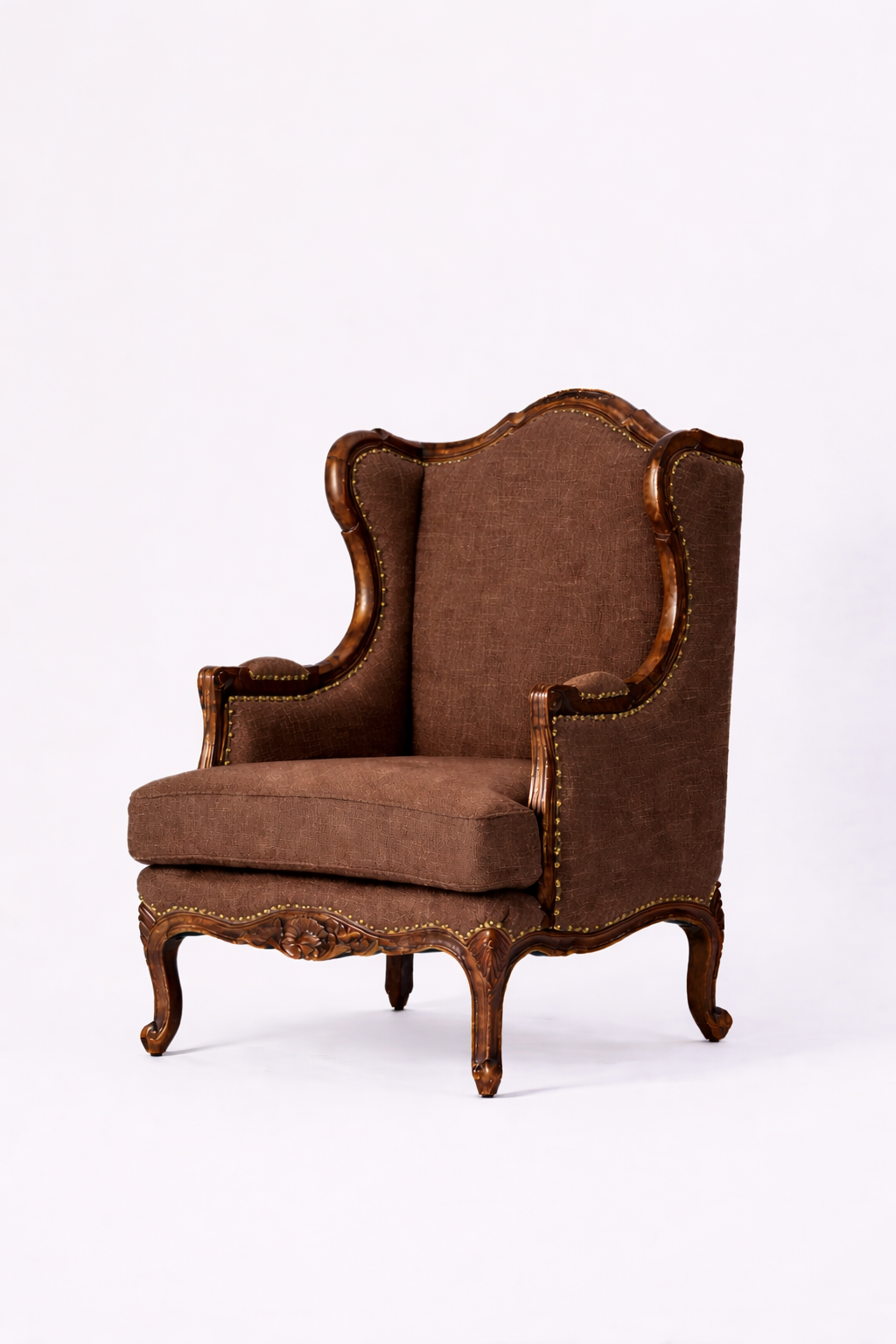 The Montclair Heritage Wingback Armchair features plush upholstery, a high back, and carved solid wood legs and trim in a vintage brown finish, showcased against a plain white background.